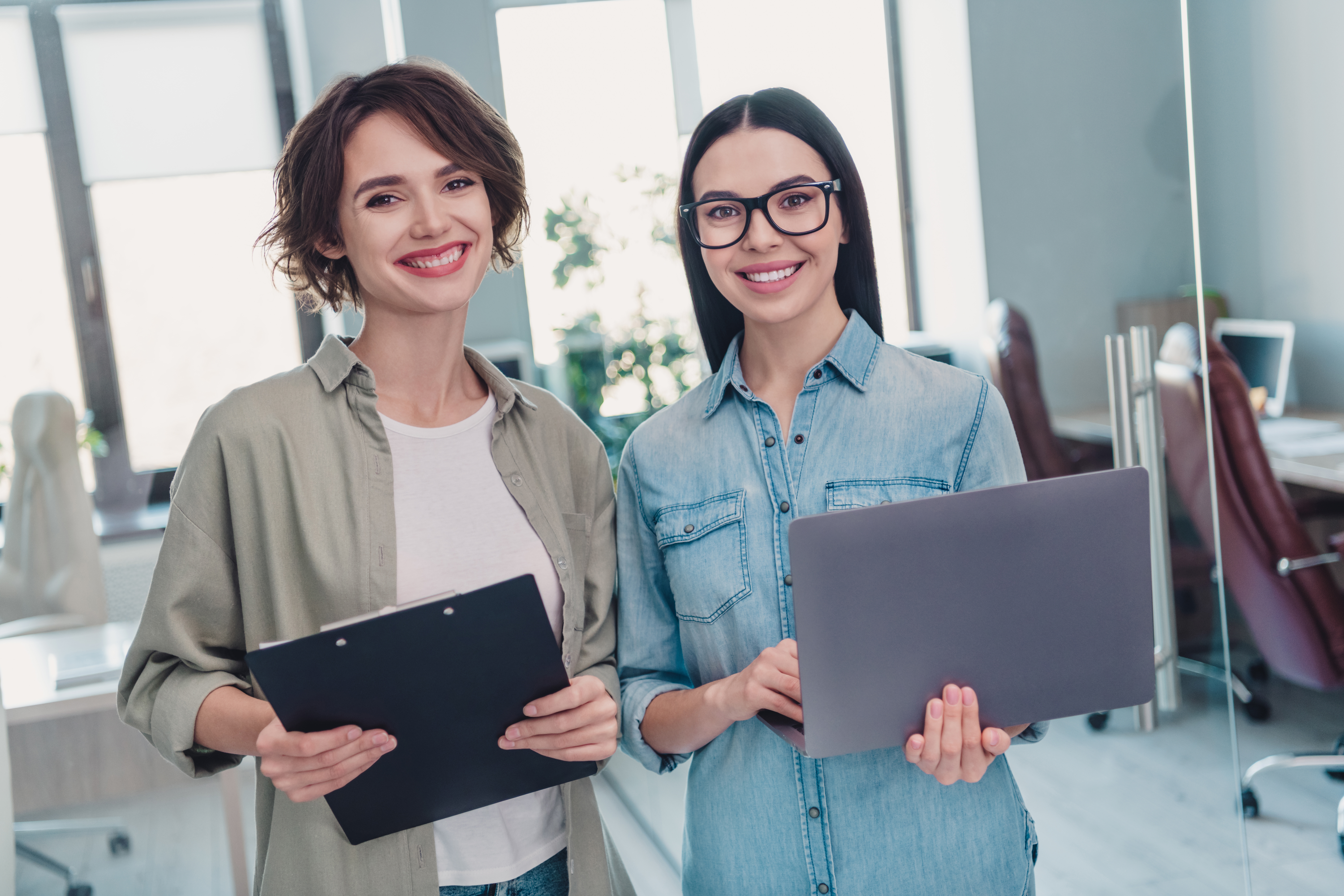 Two young cheerful marketing interns holding laptops.